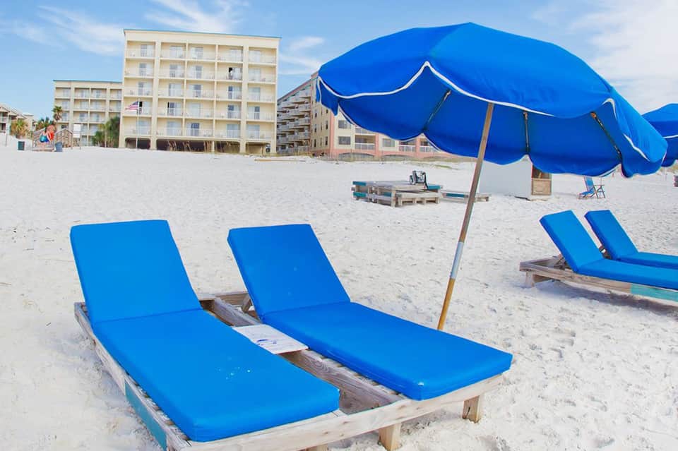 Sandy beach with blue lounge chairs, umbrellas, and beachfront hotel buildings