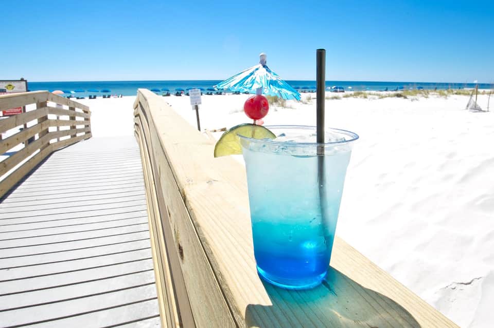 Blue tropical cocktail with lime and umbrella on wooden beach deck overlooking ocean