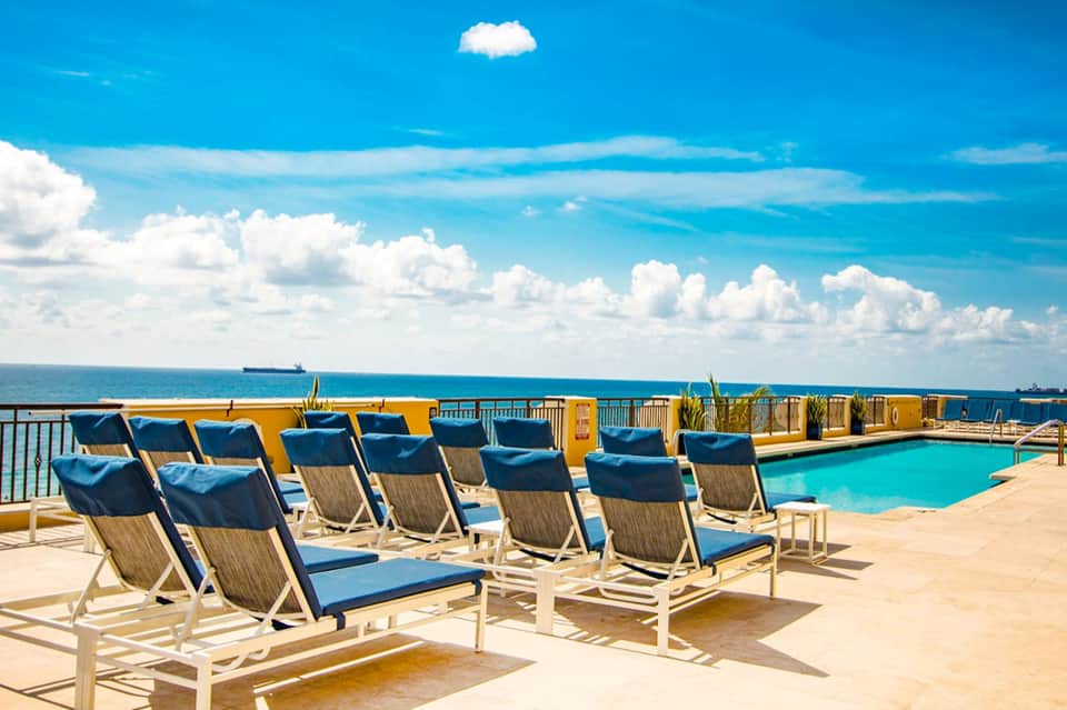 Outdoor deck lounge chairs with blue cushions overlooking a turquoise pool and ocean horizon