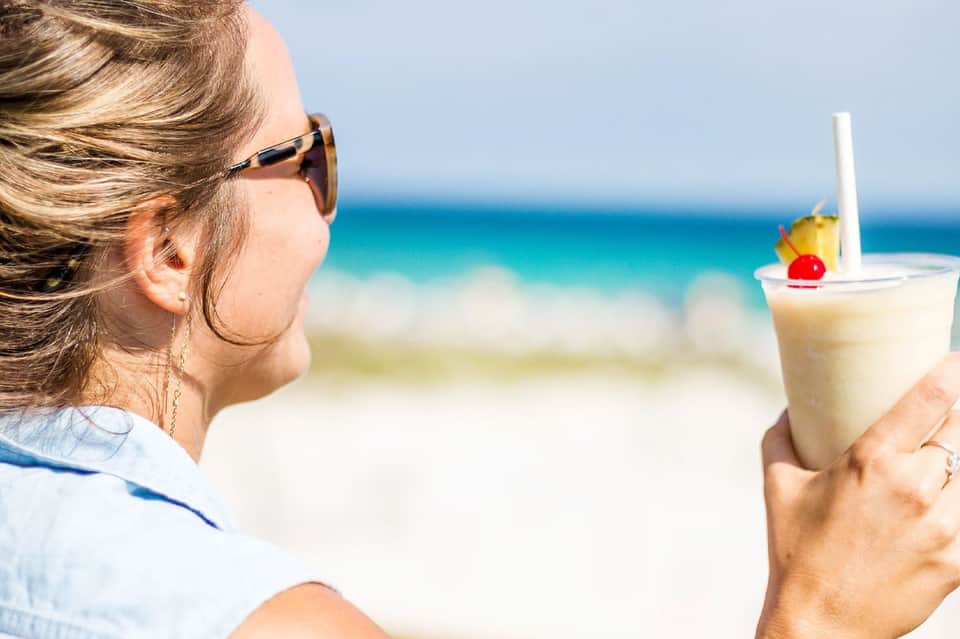 Woman in sunglasses holding tropical cocktail while enjoying ocean view from beach