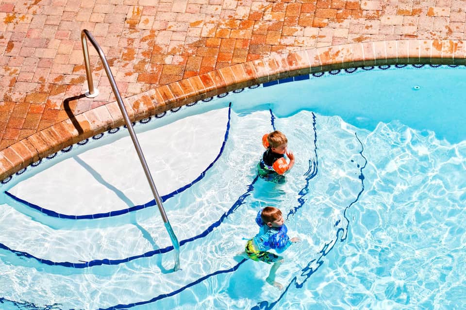 Young children in swimming pool with lane dividers and brick deck surrounding