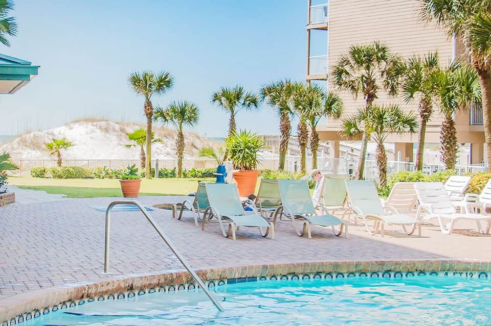 Resort pool with lounge chairs and palm trees, beachfront buildings in background