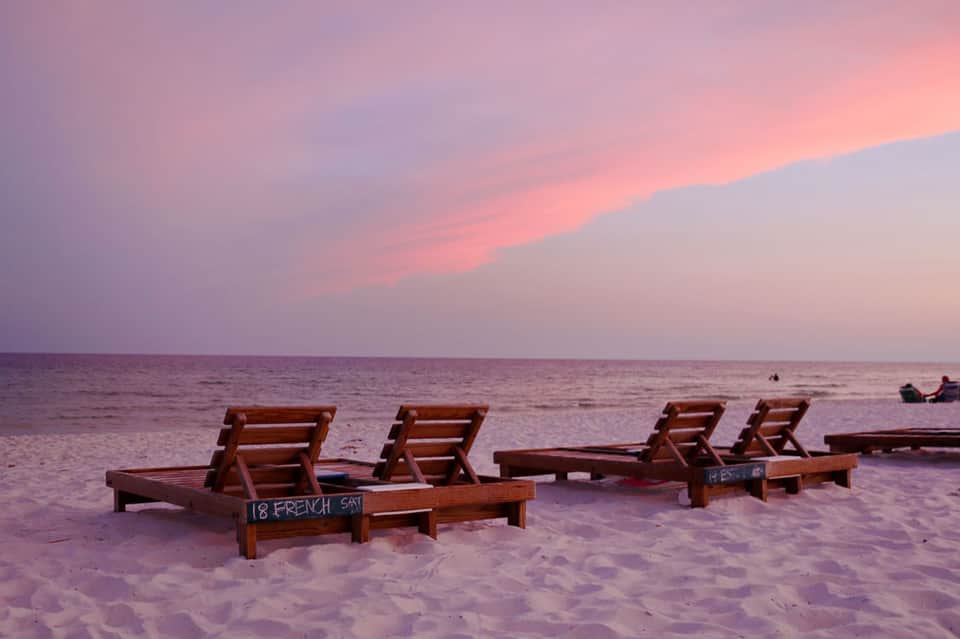 Wooden beach loungers on sand at sunset with ocean horizon and pink sky