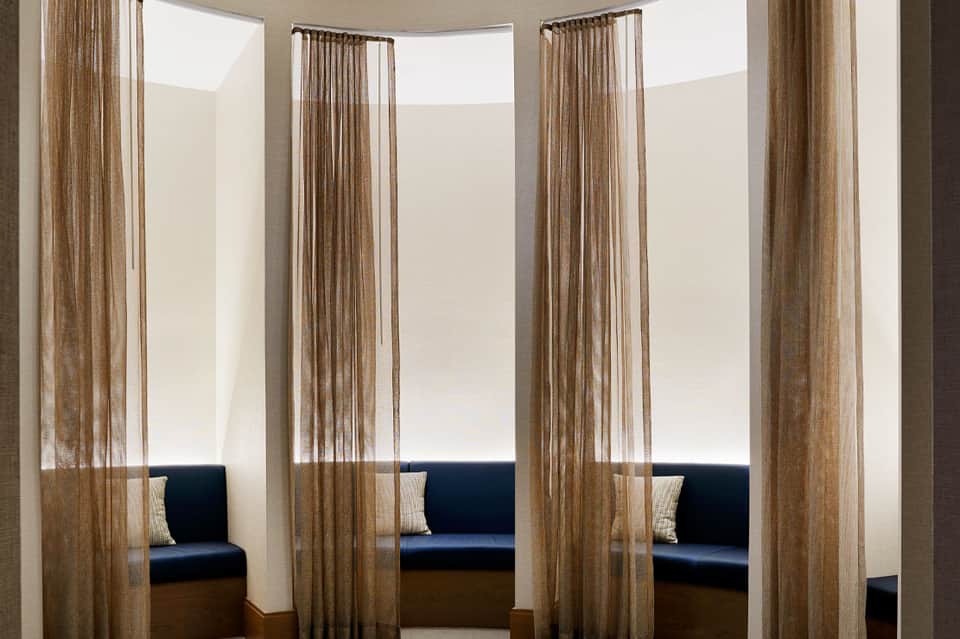 Modern spa relaxation room with sheer curtains separating private seating alcoves with navy cushions