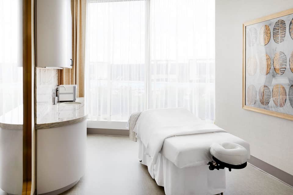 Minimalist spa treatment room with white massage bed, round sink, and floor-to-ceiling windows