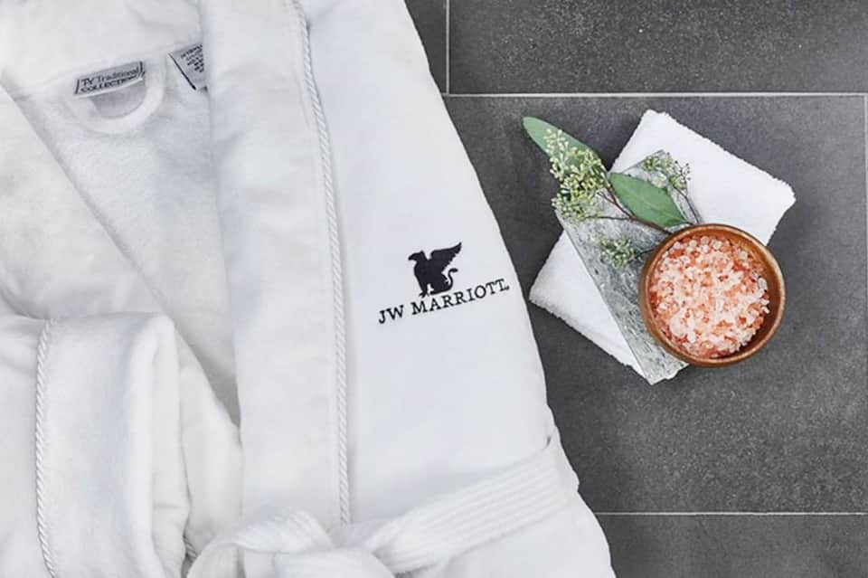 JW Marriott white bathrobe with logo displayed next to spa salt and decorative greenery