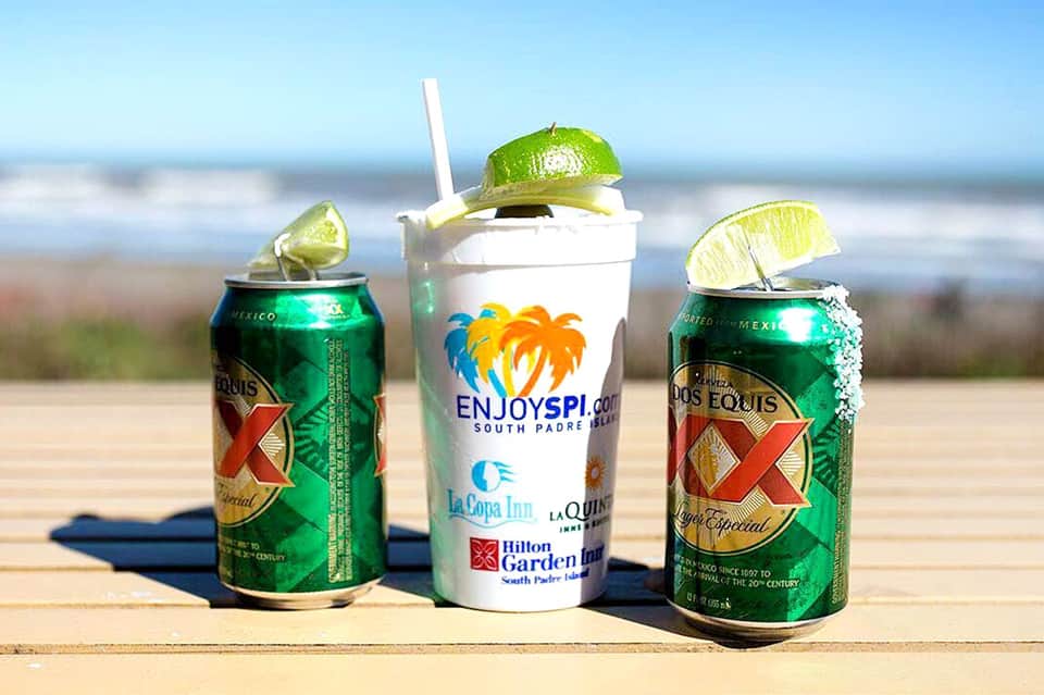 Mexican beers and tropical drink with lime garnish on beach table with ocean background