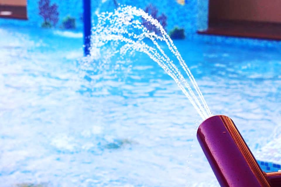 Purple pool noodle spraying water into bright blue swimming pool
