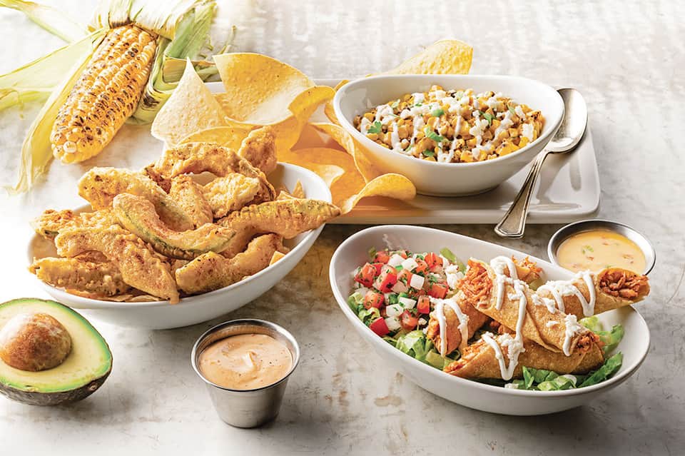 Fried chicken, tacos, corn, and side dishes on white plates with condiments
