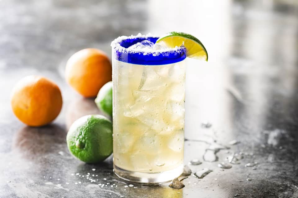 Margarita cocktail with blue salt rim and lime garnish, surrounded by fresh citrus fruits