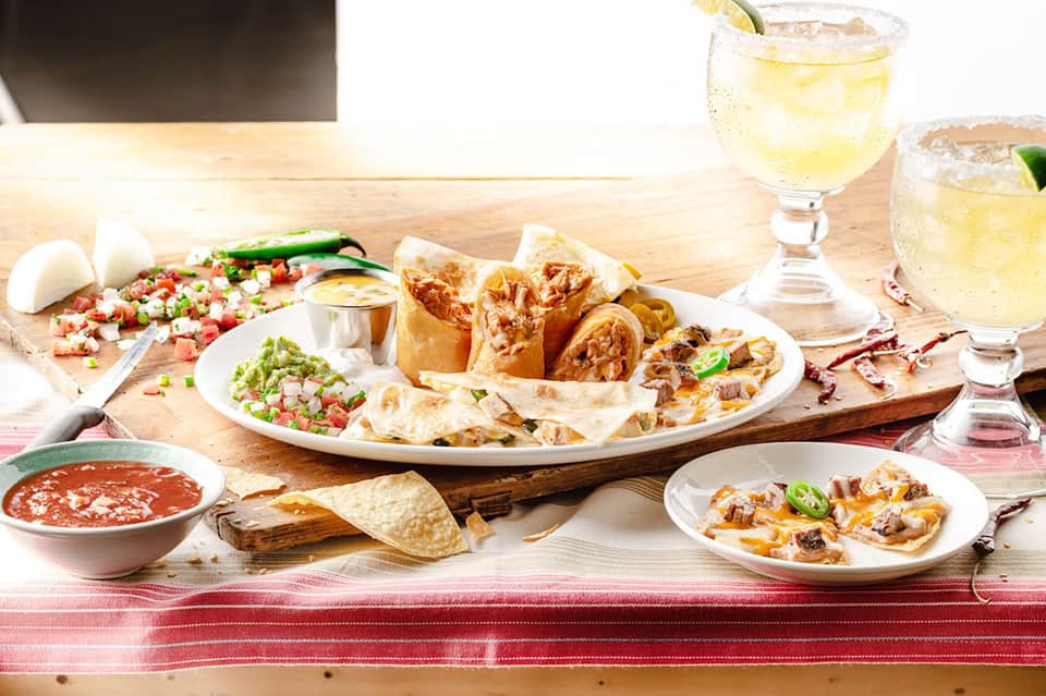 Mexican appetizers and drinks on wooden table with salsa and garnishes
