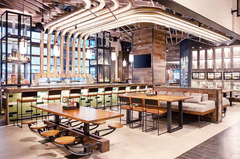 Modern hotel dining area with curved wood ceiling, bar seating, and large windows overlooking water