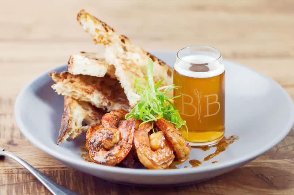 Grilled shrimp and toast appetizers on a plate with a beer glass on wooden table