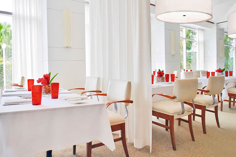 Elegant white banquet hall with round tables, red candles, and wooden chairs
