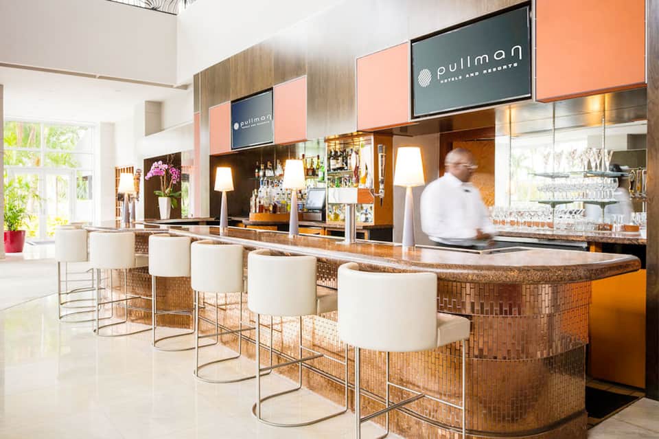 Modern hotel bar with copper accents, white bar stools, and bronze shelving