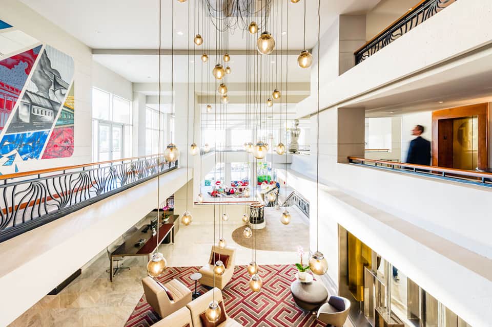 Modern hotel atrium with gold pendant lights, white railings, and colorful artwork on walls