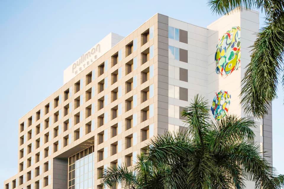 Tall hotel building with tan facade and colorful artistic murals, palm trees visible