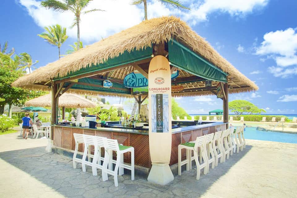 Thatched-roof beachfront bar with white seating and palm trees