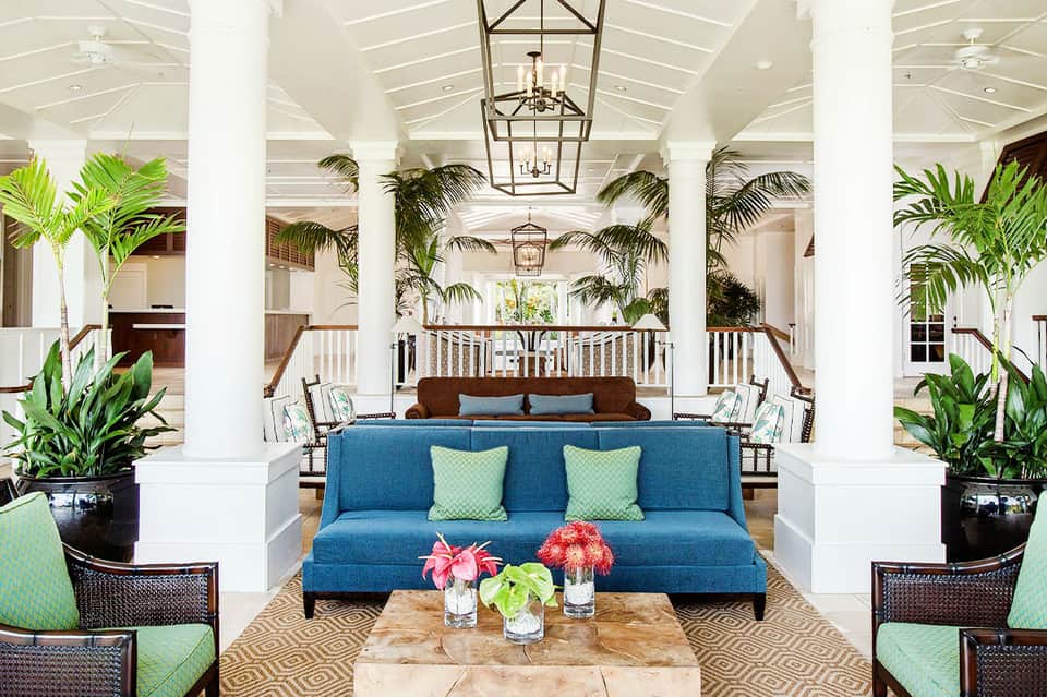 Modern covered pavilion with white columns, blue sofa, tropical plants, and elegant furnishings