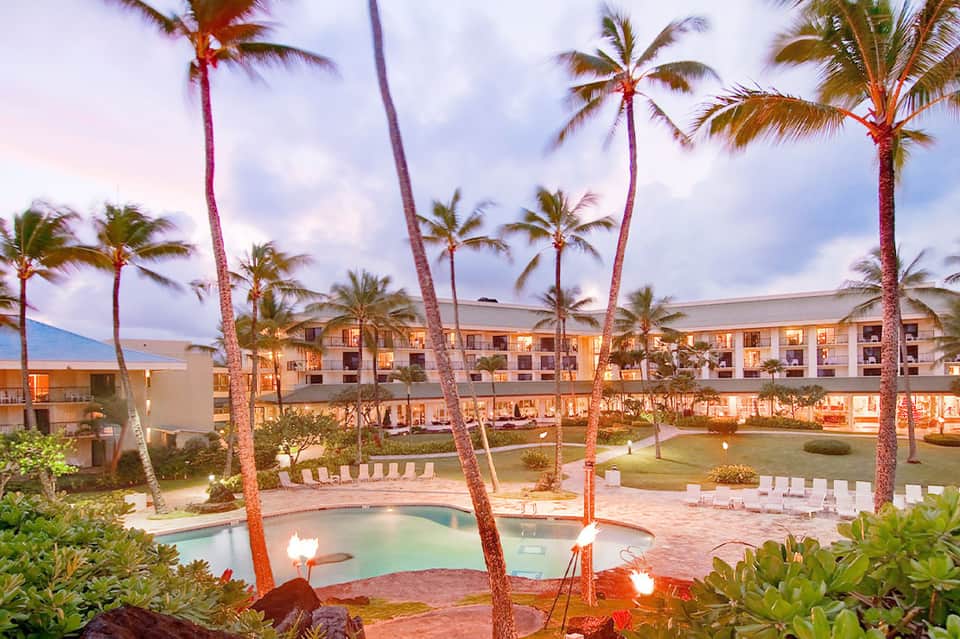 Beachfront resort at dusk with illuminated pool, palm trees, and manicured lawn