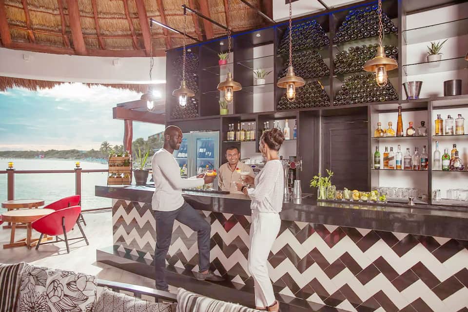 Modern waterfront bar with geometric patterns, hanging lights, and ocean view