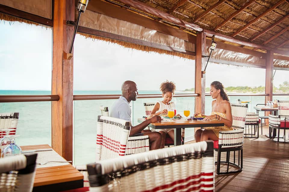 Overwater dining pavilion with three guests enjoying tropical drinks and meals overlooking turquoise lagoon