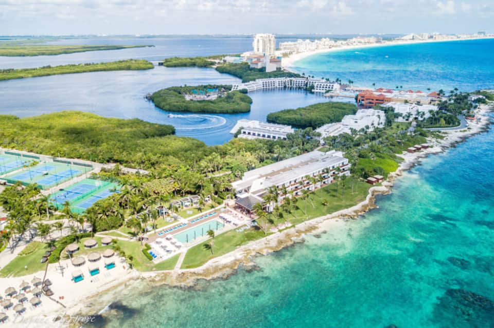 Aerial view of beachfront resort with pools, mangrove islands, and Caribbean coastline
