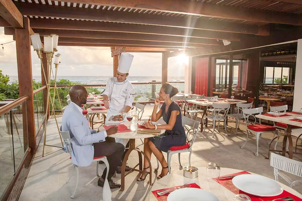 Chef serving dinner to guests on a beachfront terrace restaurant with ocean view
