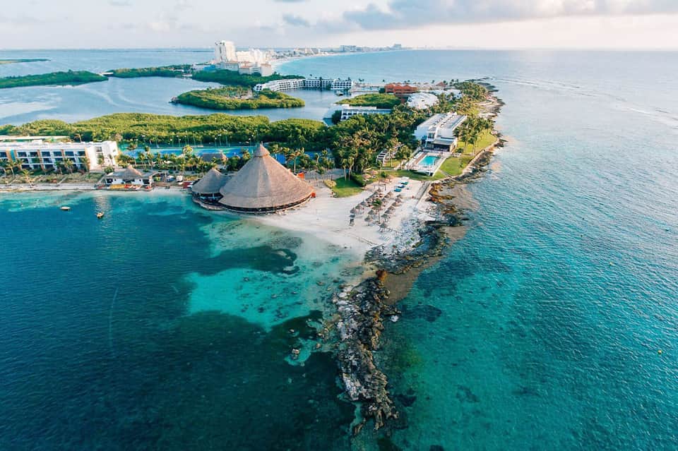Aerial view of beachfront resort with turquoise waters and thatched-roof pavilion