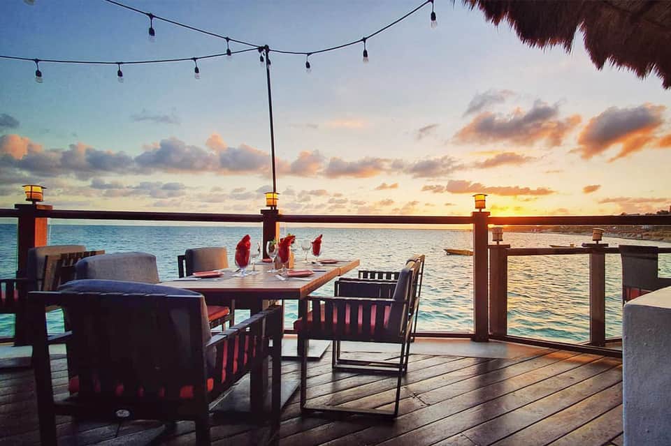 Waterfront dining table set at sunset with ocean view and string lights overhead