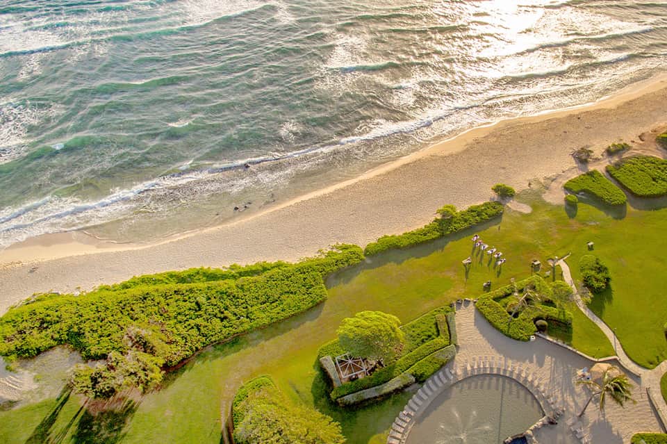 Aerial view of manicured beachfront resort grounds with circular structure and ocean waves