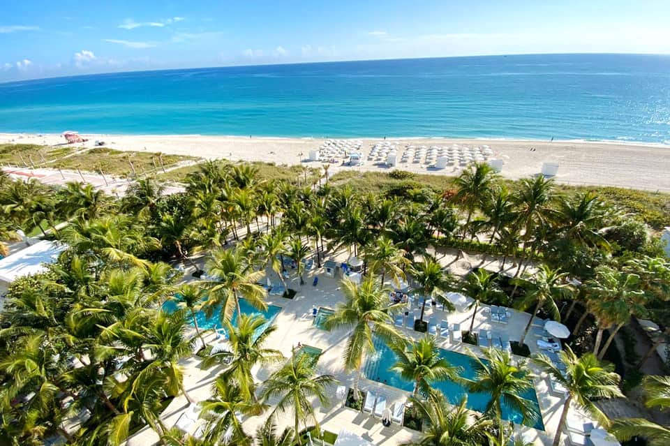 Beachfront resort with pools, palm trees, and white umbrellas overlooking turquoise ocean