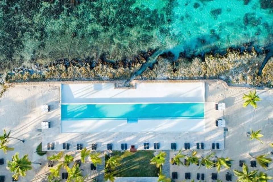 Aerial view of modern beachfront pool with turquoise water overlooking coral reef and ocean