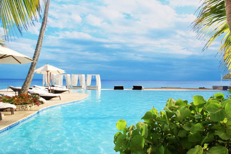 Luxury beachfront infinity pool overlooking the ocean with palm trees and cabanas