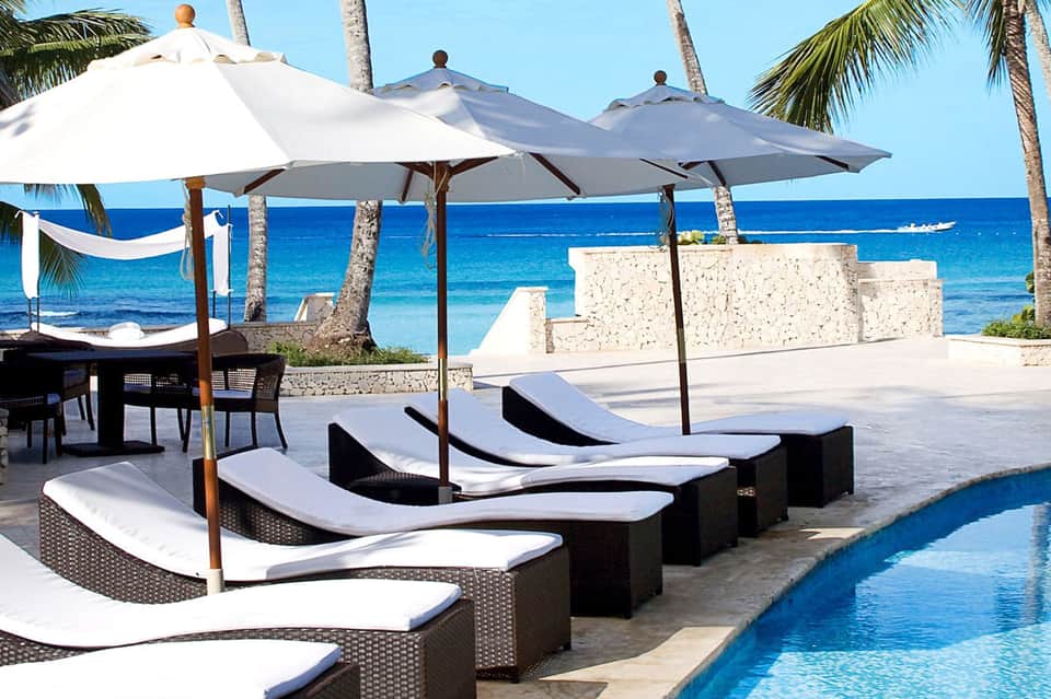 Beachfront lounge area with black rattan sunbeds, white umbrellas, and ocean view