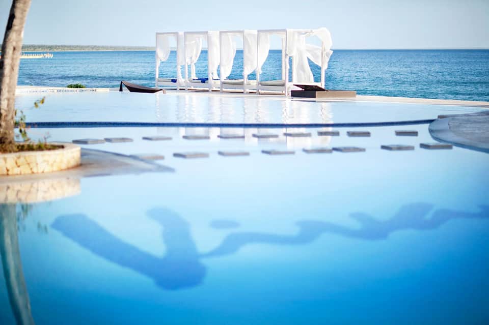 Infinity pool blending with ocean horizon, white cabanas, and beach lounge chairs with ocean view