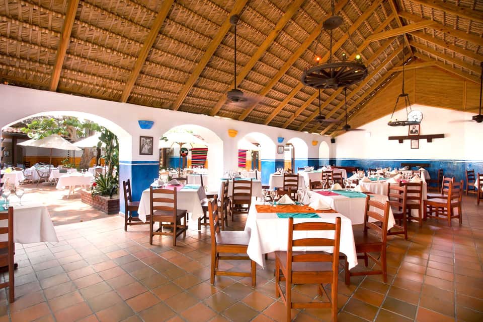 Elegant dining room with white tablecloths, wooden chairs, arched ceilings, and traditional Spanish colonial decor