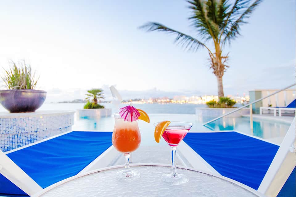 Tropical rooftop bar with cocktails, ocean view, palm trees, and blue lounge chairs at seaside hotel