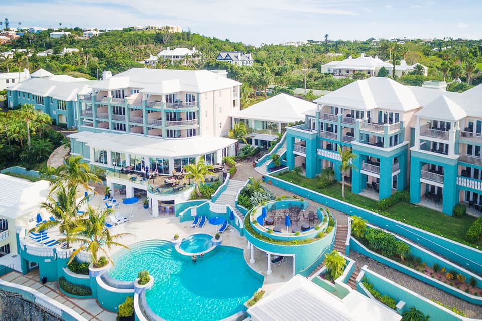 Aerial view of colorful turquoise and white resort buildings with multiple pools and surrounding lush greenery
