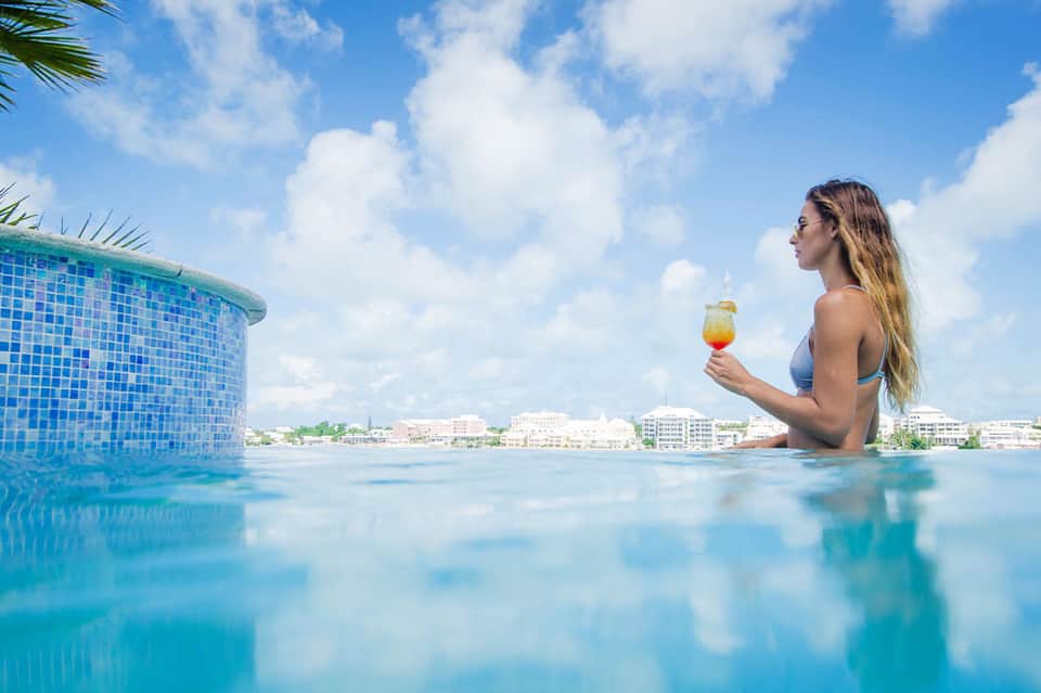 Woman swimming in bright blue pool holding tropical drink