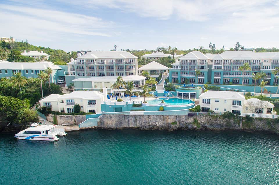 Waterfront resort with turquoise pools, pastel-colored buildings, and a docked yacht