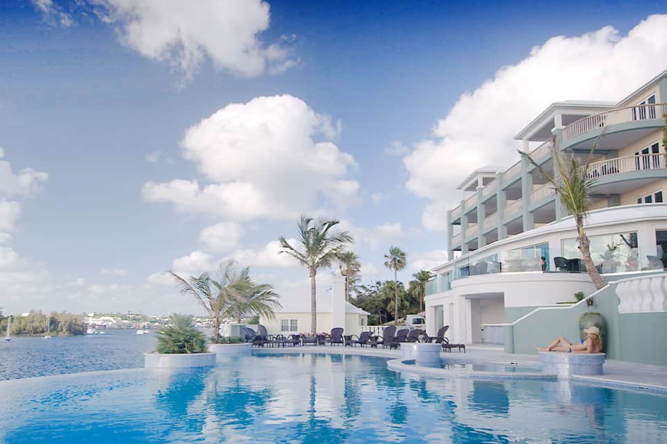 Waterfront resort pool with palm trees, lounge chairs, and multi-story white building overlooking bay