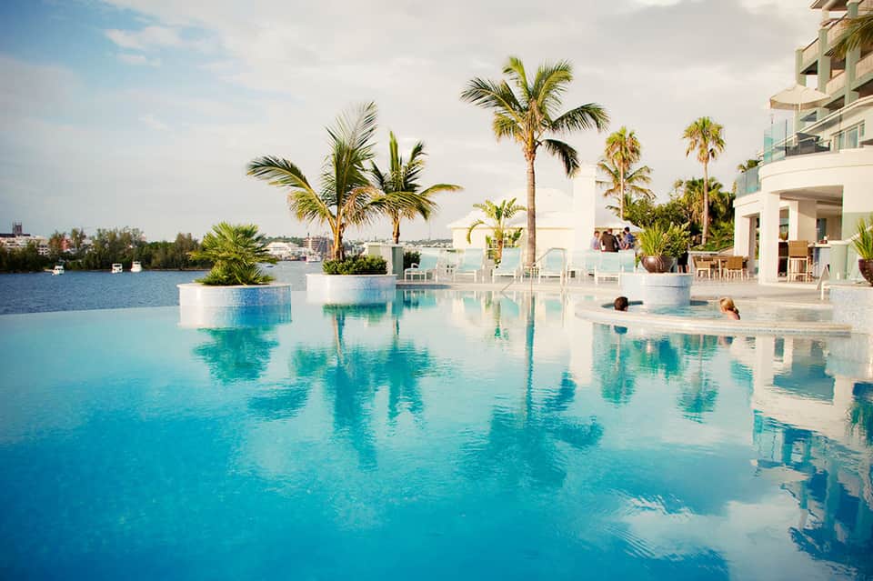 Luxury infinity pool with palm trees and waterfront resort building