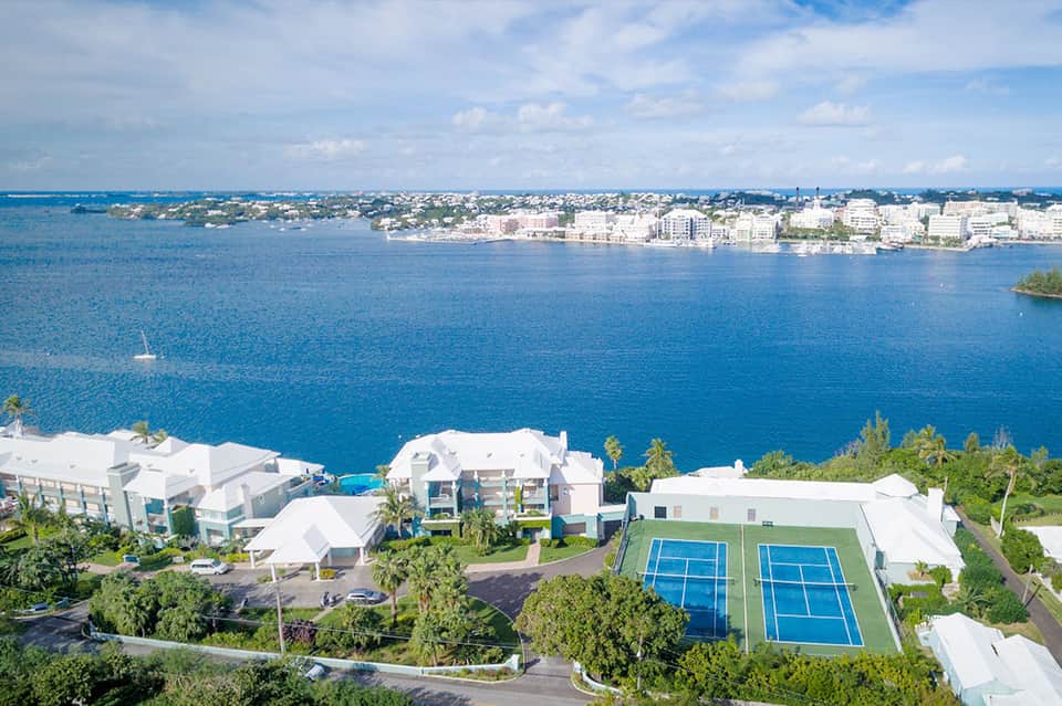 Aerial view of a beachfront resort with white buildings, blue tennis courts, and ocean view