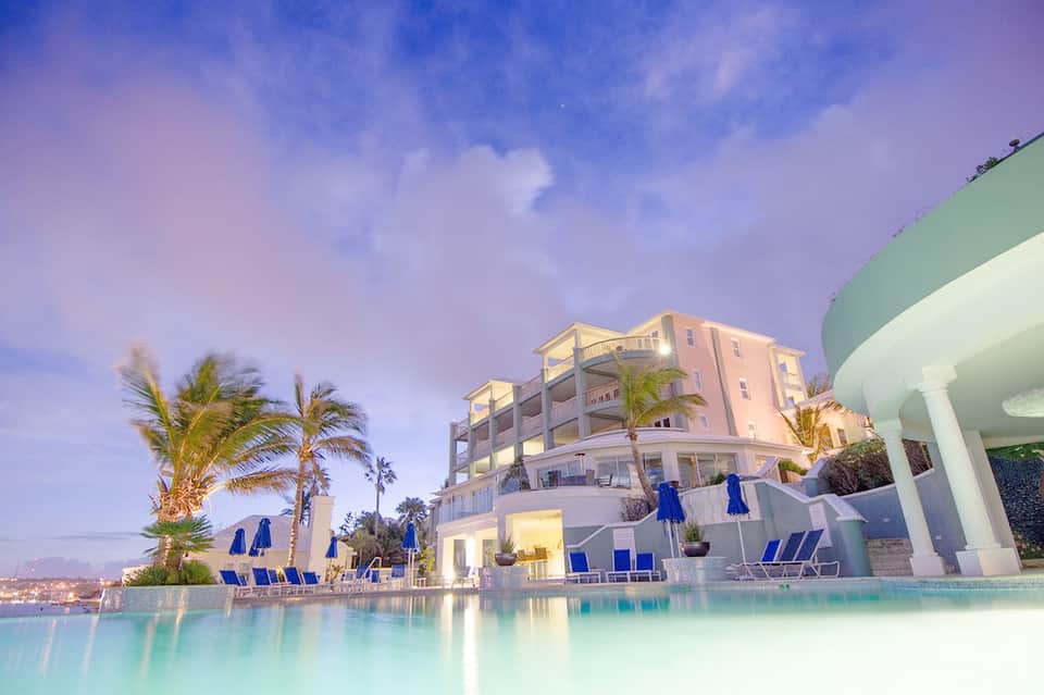 Luxury resort with illuminated pink building, palm trees, and glowing infinity pool at dusk