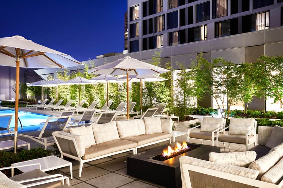 Luxury resort pool deck with loungers, umbrellas, fire pit, and modern high-rise building at dusk