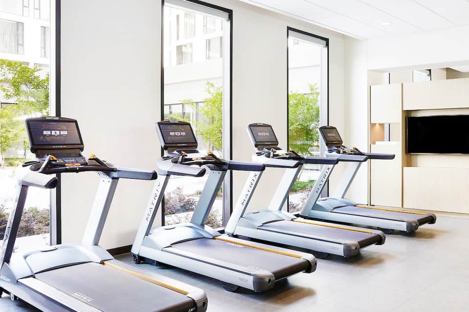 Modern fitness center with white treadmills lined up facing large windows overlooking tropical landscape