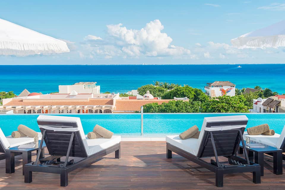 Pair of lounge chairs on wooden deck overlooking infinity pool and tropical ocean horizon