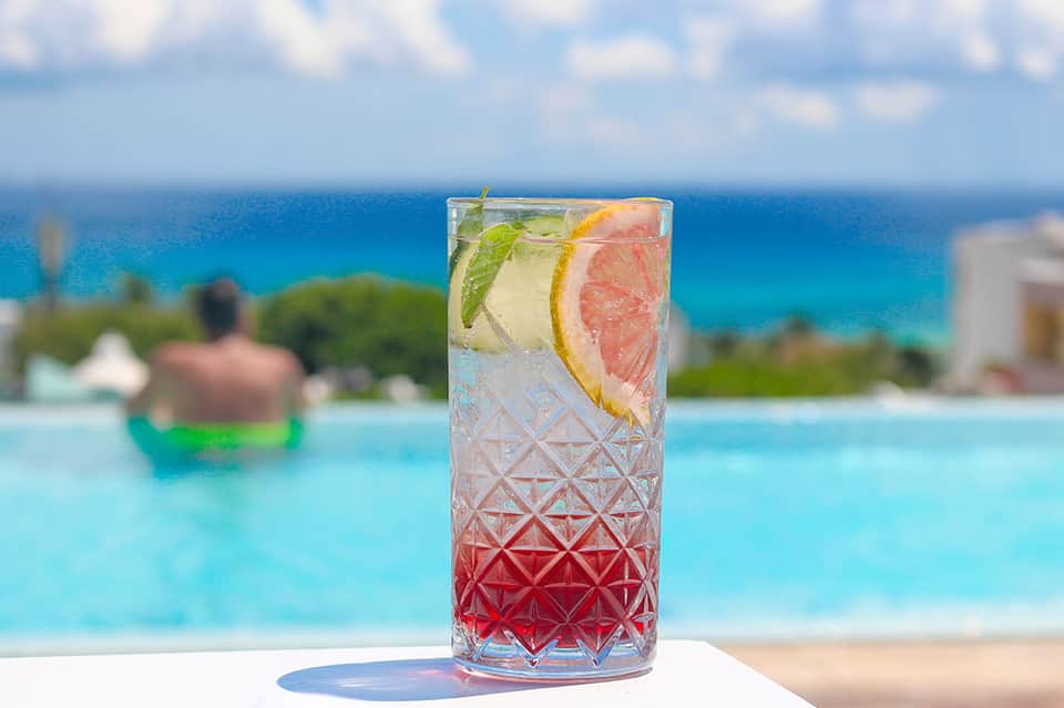 Tropical cocktail with grapefruit and citrus garnish overlooking turquoise ocean and beach