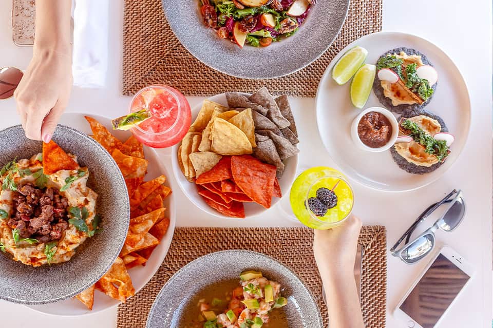 Overhead view of colorful Mexican dishes with chips, tacos, and cocktails